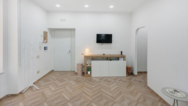 A hotel room with a wooden floor, a TV mounted on the wall, a small table, and a cabinet. - Apartment 'A casa re nonni' with Balcony, Wi-Fi and Air Conditioning (Naples)