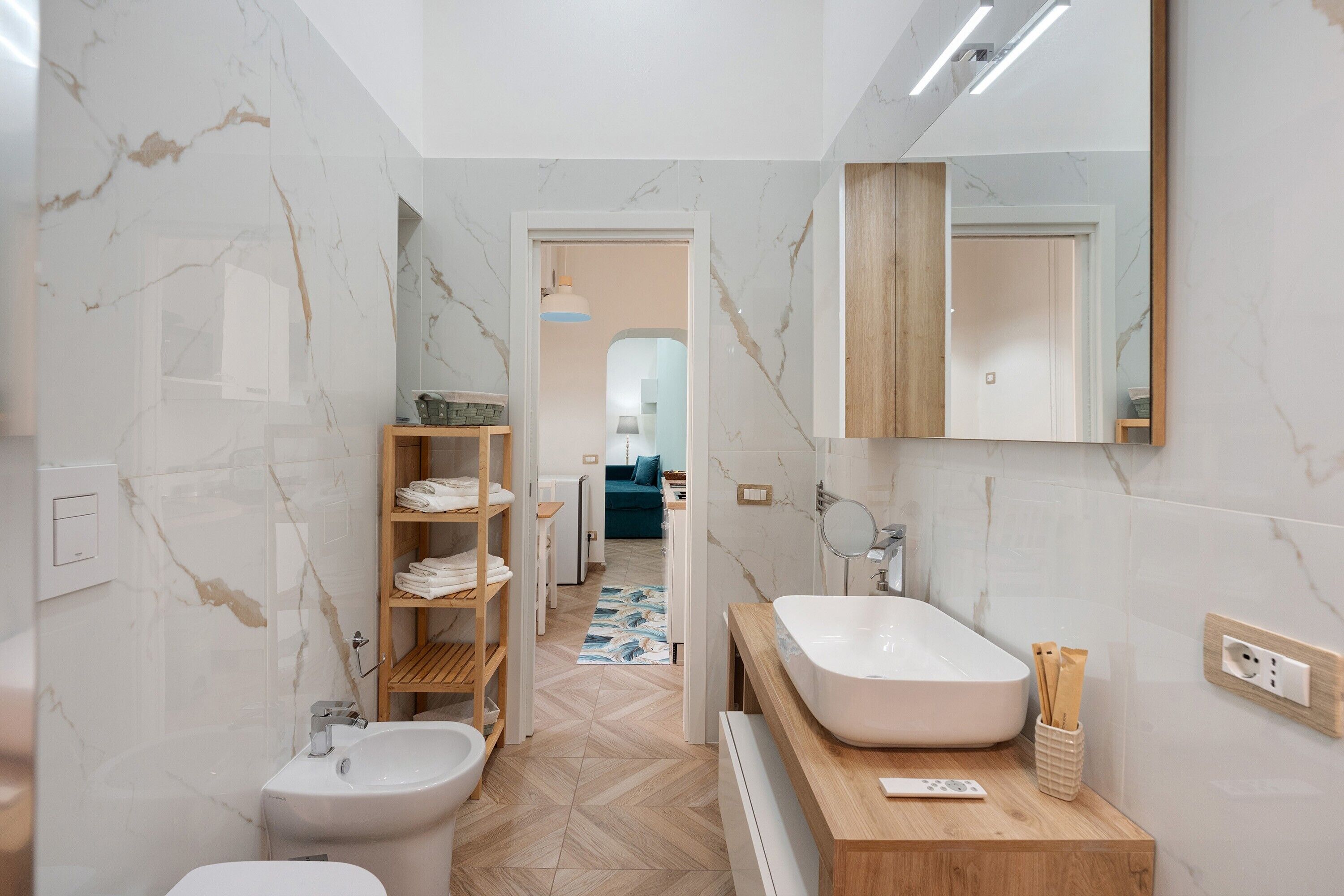 Ein modernes Badezimmer mit Marmorwand, einem Holzkosmetikschrank, einem freistehenden Waschbecken und einer eingebauten Toilette.