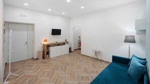 A room with a herringbone floor, a teal sofa, a small table, a TV mounted on the wall, and a door leading to a bathroom. - Apartment 'A casa re nonni' with Balcony, Wi-Fi and Air Conditioning (Naples)