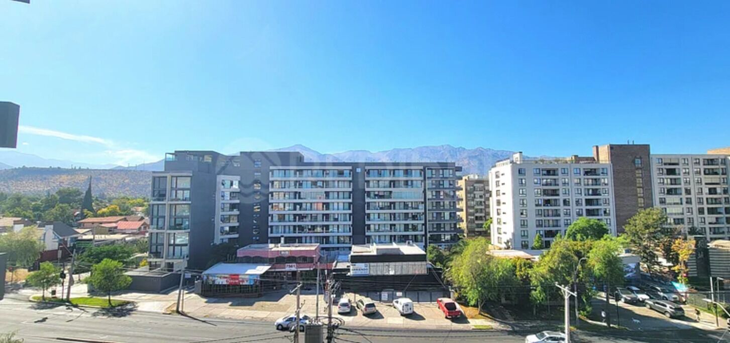Un immeuble à plusieurs étages doté d’une architecture moderne, caractérisé par un mélange de façades en verre et en brique, et un parking situé au premier plan.