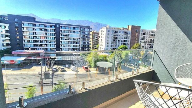 A balcony with a view of a parking lot and buildings, a satellite dish, and a chair. - Rbk Estudio exclusivo sector Las Condes (Las Condes)