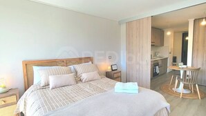 A bedroom with a bed, bedside table, and a view into the kitchen. - Rbk Estudio exclusivo sector Las Condes (Las Condes)