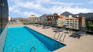 A rooftop pool with sun loungers and a view of buildings and mountains. - Rbk Estudio exclusivo sector Las Condes (Las Condes)