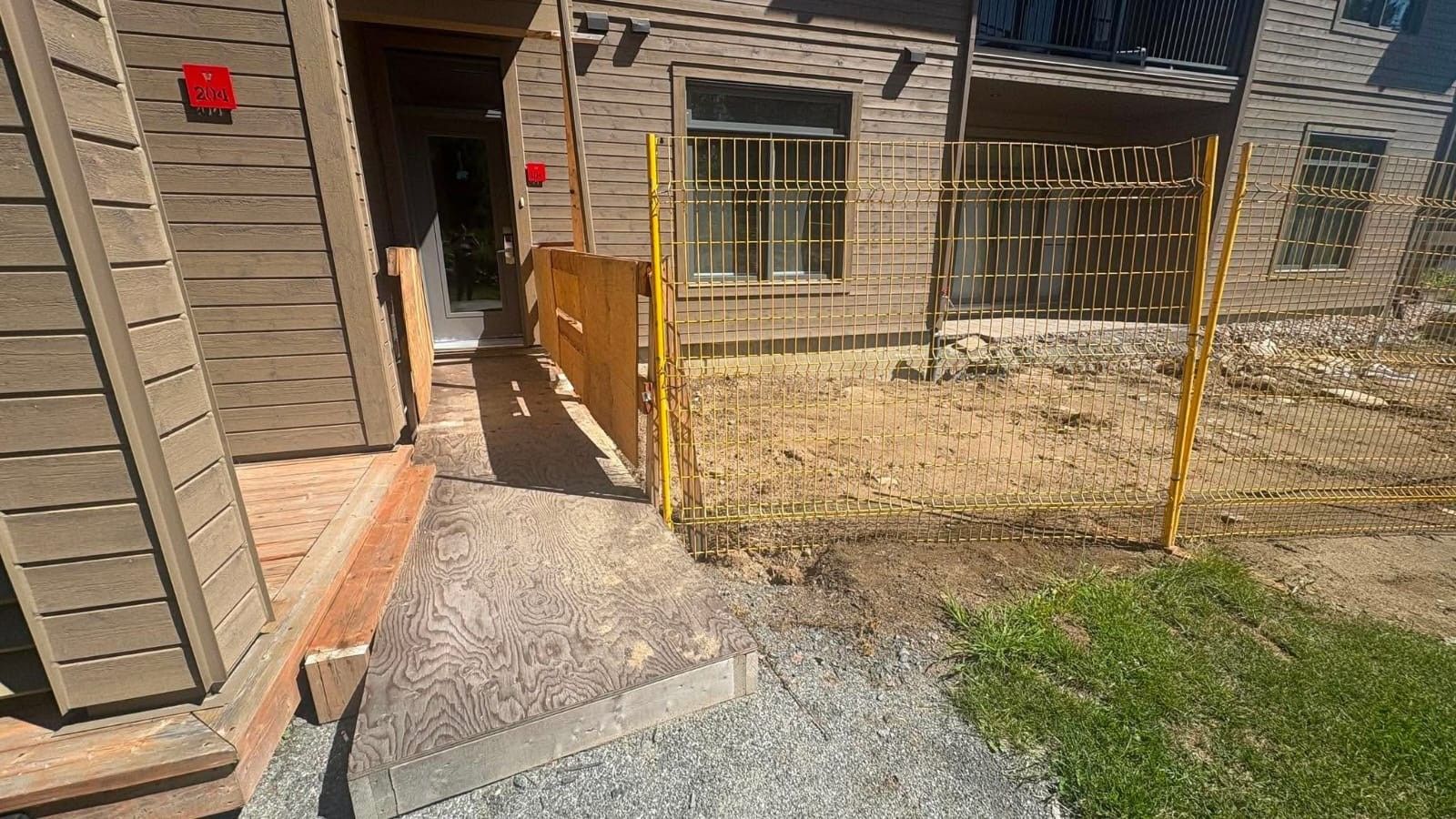 Entrada de un edificio con una puerta de madera, un portón metálico y un camino empedrado que lleva a una zona cubierta de césped.