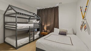 Un lit superposé avec une échelle, une table de chevet avec une lampe, un lit avec des oreillers et un mur décoré de drapeaux de différentes équipes sportives.