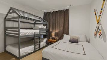 Una cama litera con escalera, una mesita de noche con lámpara, una cama con almohadas y una pared decorada con banderas deportivas.