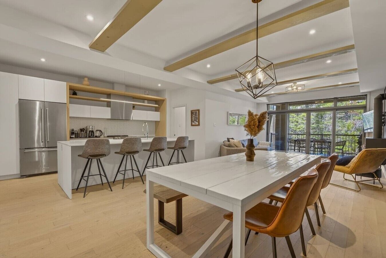 Una cocina moderna con una isla central, taburetes de bar y una zona de comedor con una mesa larga y sillas.