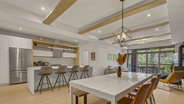 Une cuisine moderne dotée d’un îlot central, de tabourets de bar et d’un coin repas avec une longue table et des chaises.