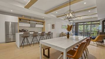 Una cocina moderna con una isla central, taburetes de bar y una zona de comedor con una mesa larga y sillas.