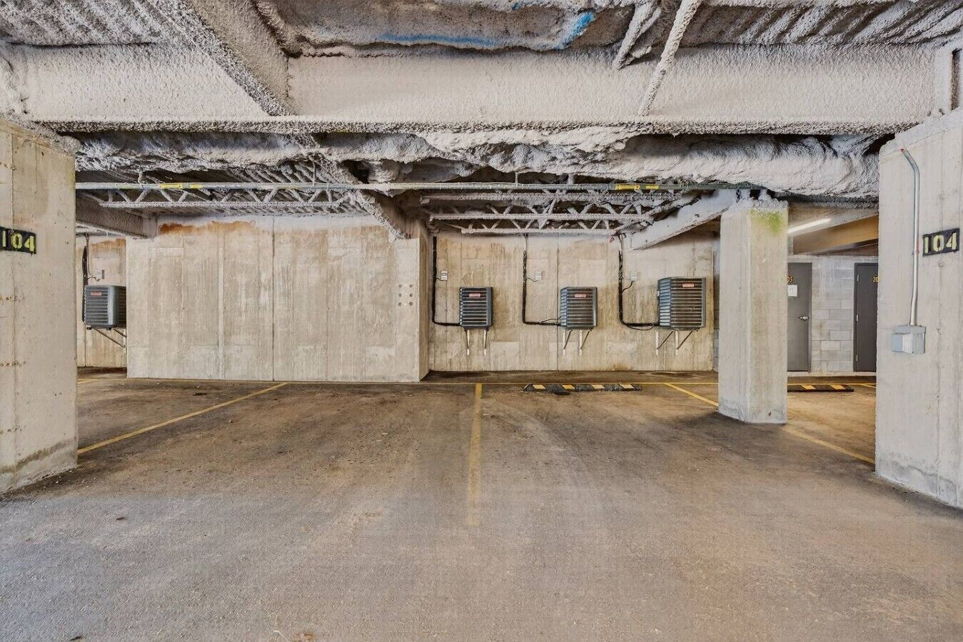 Uma garagem subterrânea com paredes de concreto, grelhas de ventilação metálicas e vagas numeradas.
