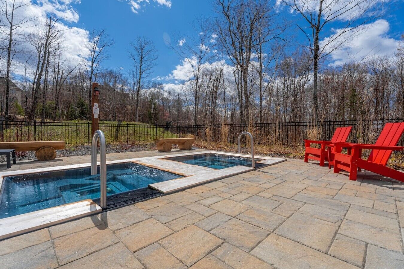 Un área de piscina con dos jacuzzis, sillas Adirondack rojas y un patio de piedra.