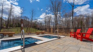 Un espace piscine doté de deux bains à remous, de chaises Adirondack rouges et d’une terrasse en pierre.