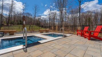 Un área de piscina con dos jacuzzis, sillas Adirondack rojas y un patio de piedra.