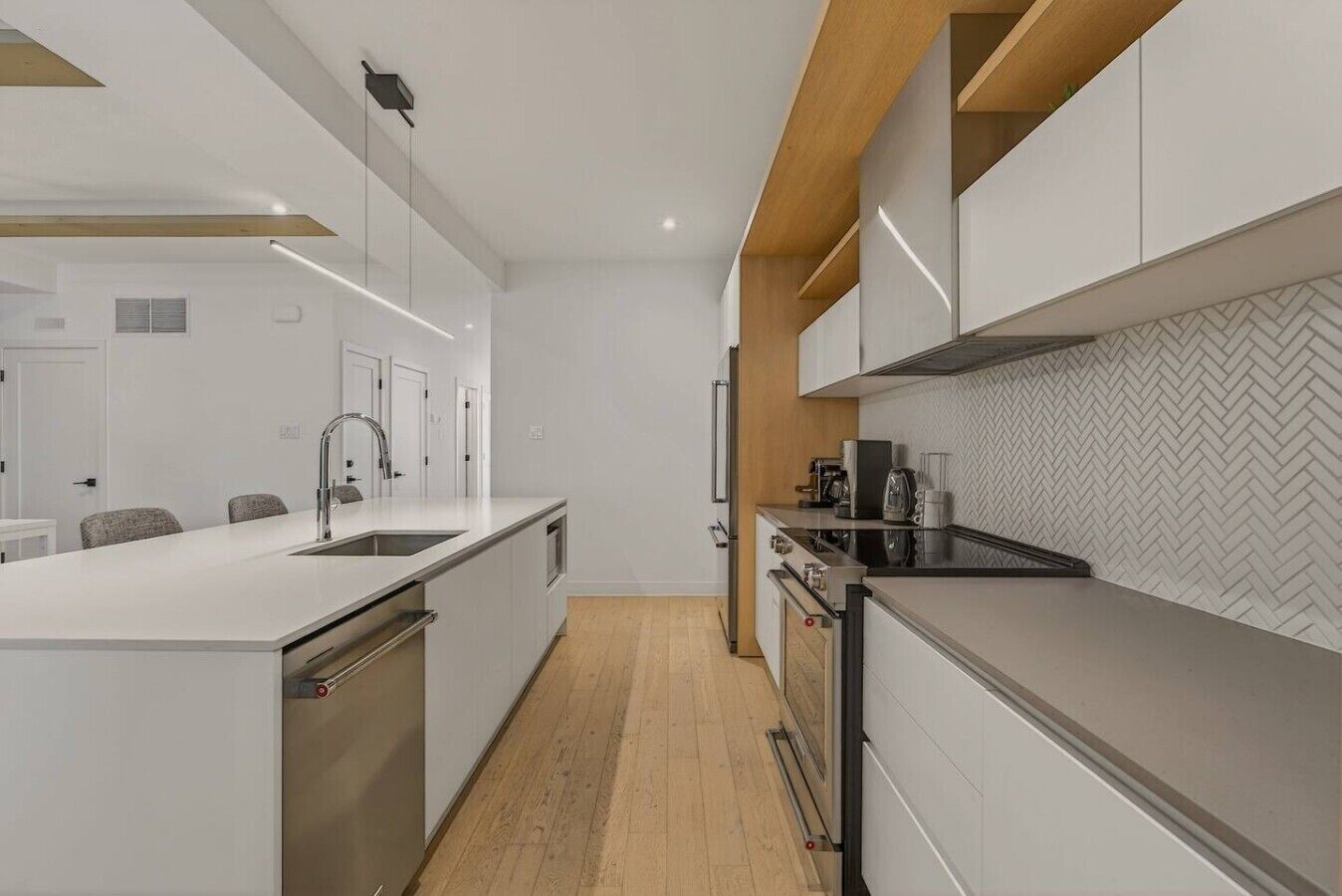 A modern kitchen with white cabinetry, a wooden floor, and a herringbone-patterned backsplash.