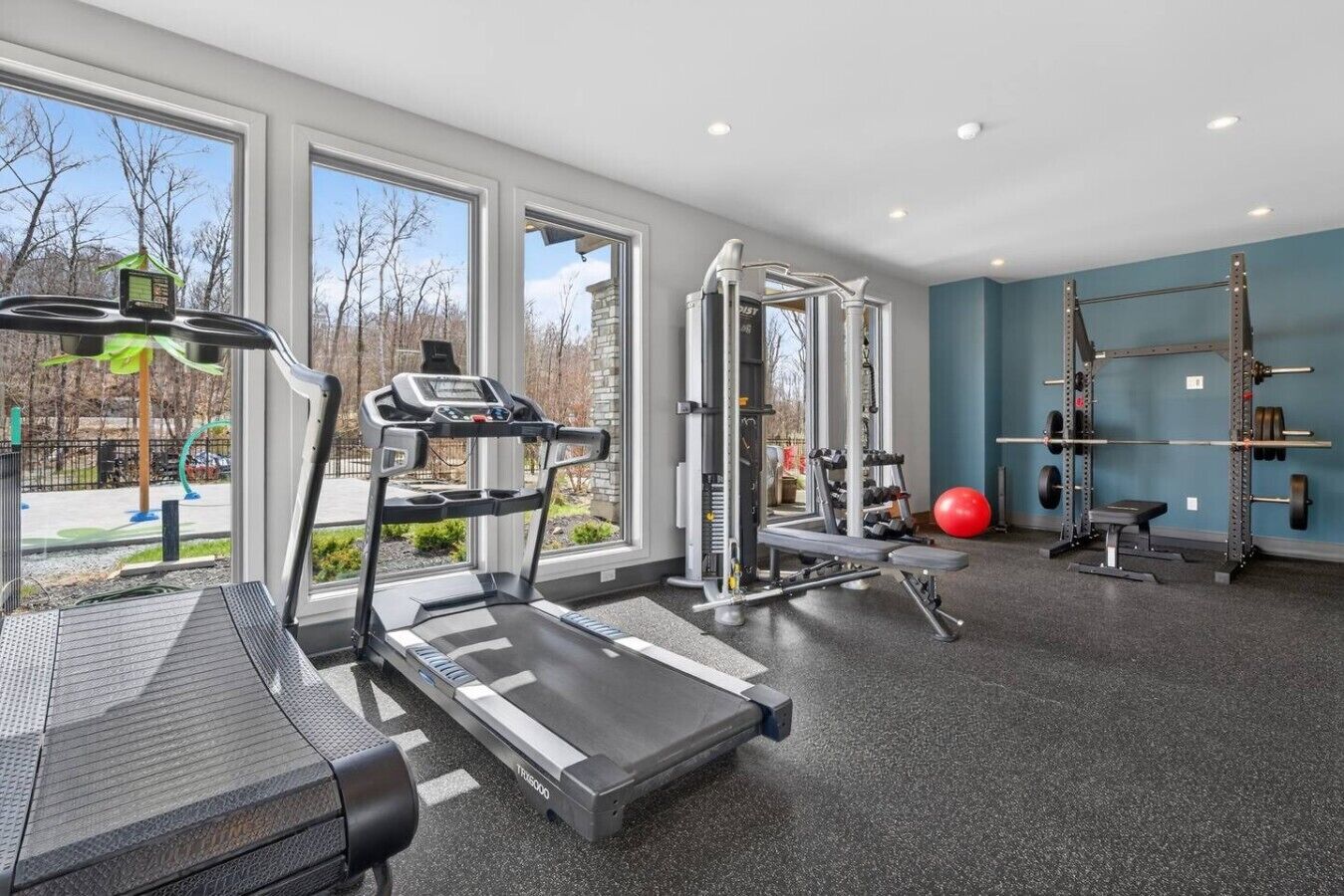 Une salle de sport équipée de tapis de course, d’appareils de musculation et d’un ballon d’exercice rouge.