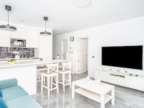 A modern kitchen with white cabinets, a built-in microwave, and a dining area with white chairs and a table. - Abedules by Interhome (Benalmádena Costa)