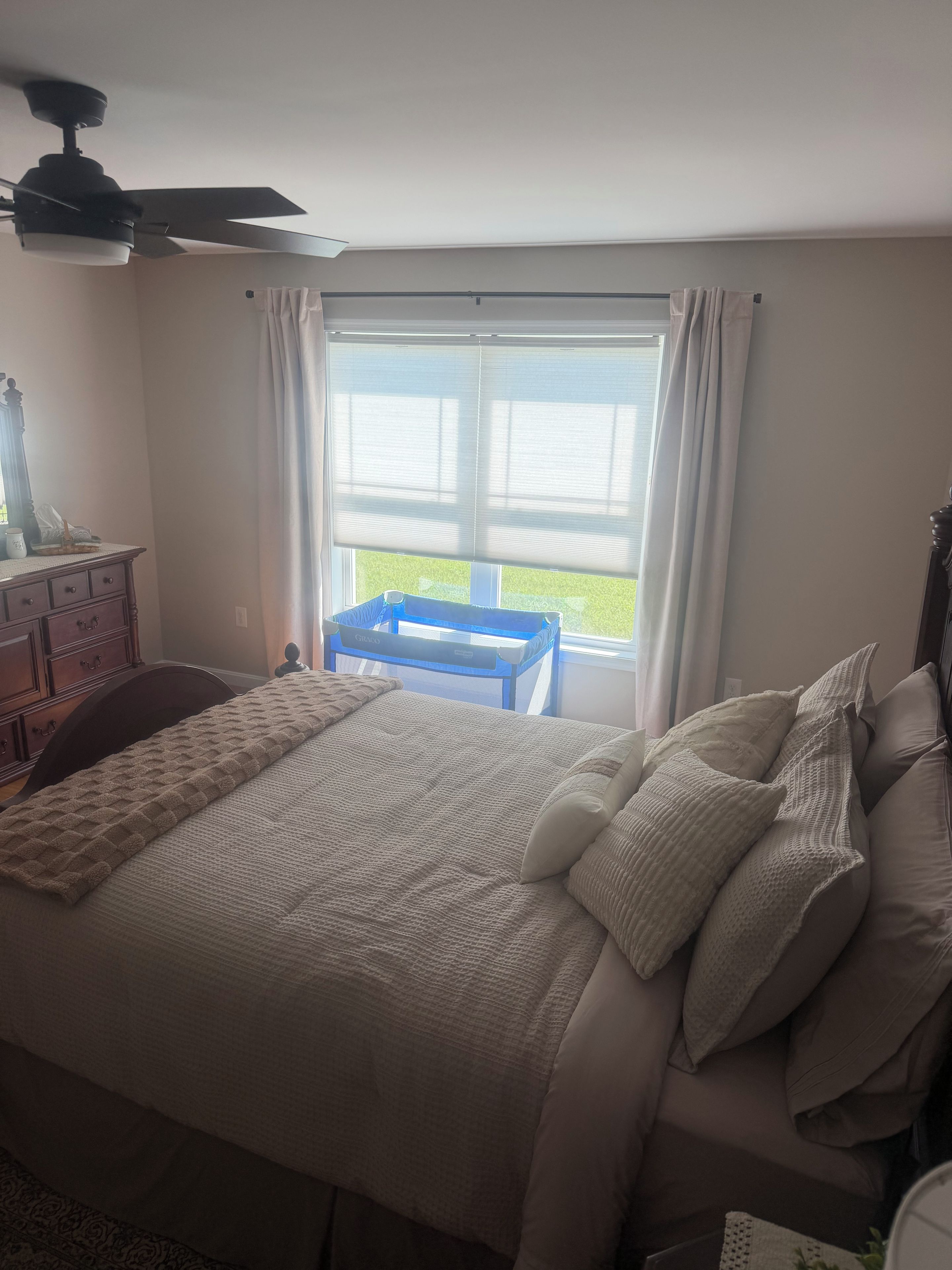 Een slaapkamer met een bed, een dressoir, een raam met gordijnen en een plafondventilator.