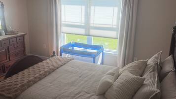 Een slaapkamer met een bed, een dressoir, een raam met gordijnen en een plafondventilator.