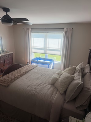 Un dormitorio con cama, cómoda, ventana con cortinas y ventilador de techo.
