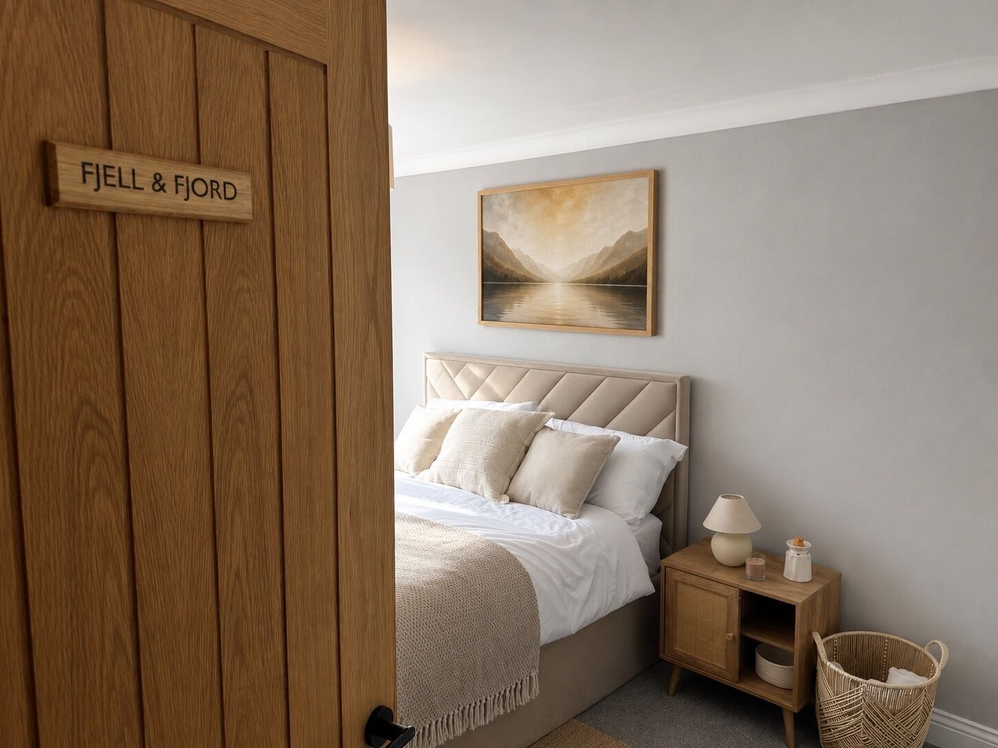 A bedroom with a bed, a nightstand, a lamp, a basket, and a painting on the wall.