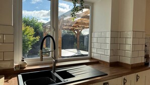 Une cuisine dotée d’un évier à deux bacs, d’un plan de travail en bois, d’un crédence carrelée blanche et d’une fenêtre donnant sur une terrasse en bois.