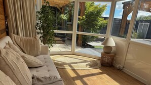 Un salon confortable avec un canapé, une lampe et une vue dégagée sur l’extérieur grâce à une grande fenêtre.