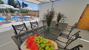 A table with a fruit platter, outdoor seating, and a pool in the background. - Olive Garden -Family Villa with Private Pool in Posedarje near Zadar (Posedarje)