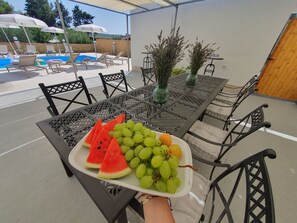 A table with a fruit platter, outdoor seating, and a pool in the background. - Olive Garden -Family Villa with Private Pool in Posedarje near Zadar (Posedarje)