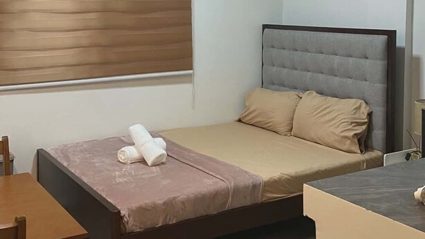 A single bed with a headboard, a wooden table, a chair, a window with blinds, an air conditioner, and a lamp. - Soothing studio with AC in lovely Olongapo City (Olongapo City)