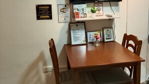 A dining area with a wooden table and chairs, a mounted television, and wall-mounted artwork. - Soothing studio with AC in lovely Olongapo City (Olongapo City)