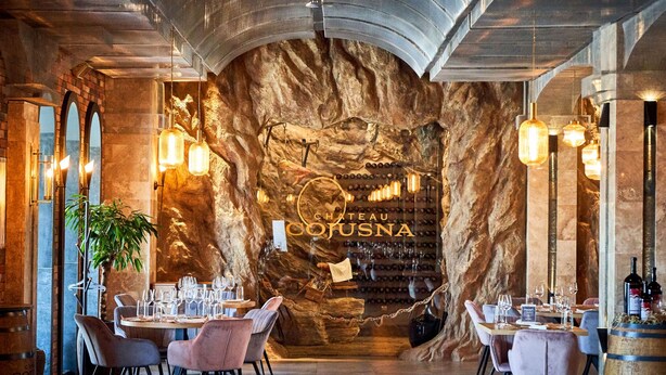 A restaurant interior with a stone wall, hanging wine bottles, and tables set for dining. - Hotel Chateau Cojusna (Cojușna)