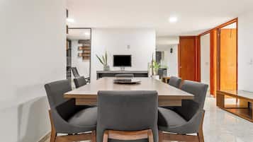 Un comedor moderno con una larga mesa de madera, seis sillas grises tapizadas, un televisor de pantalla plana y una planta en maceta.