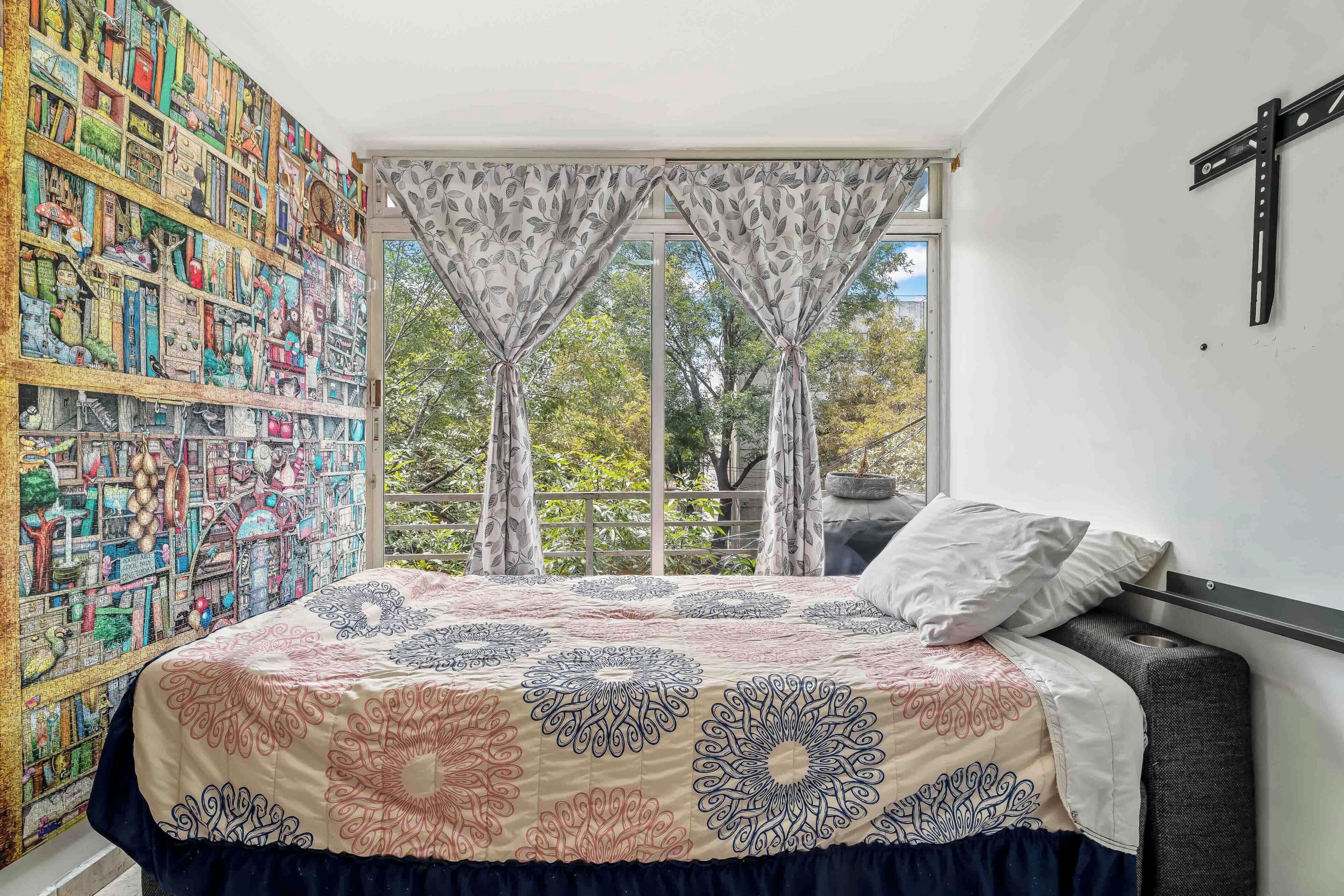 Un dormitorio con una cama, una estantería, una ventana con cortinas y una cruz en la pared.