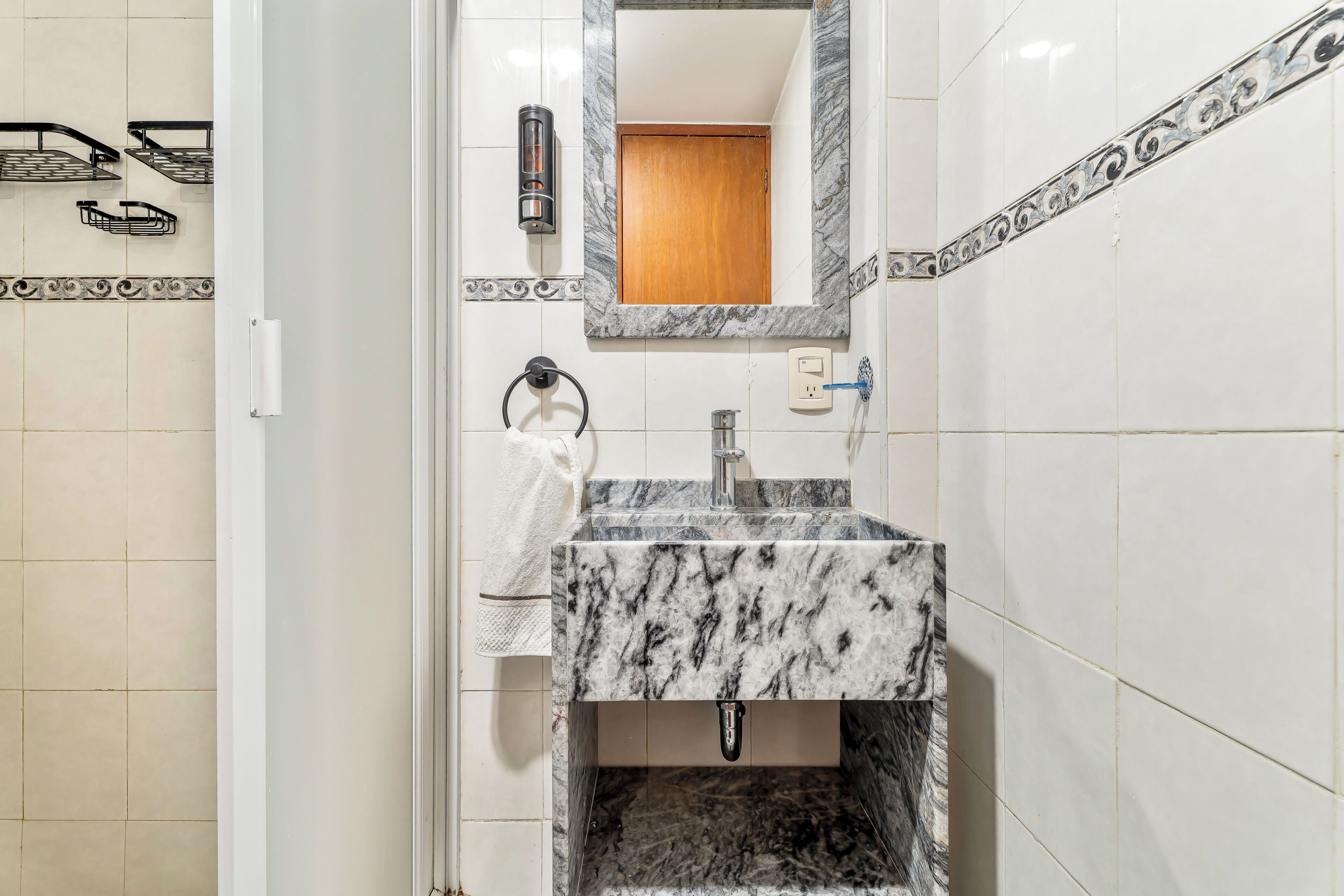 Un bagno con un lavandino in marmo, uno specchio, un portasciugamani e uno spazio doccia.