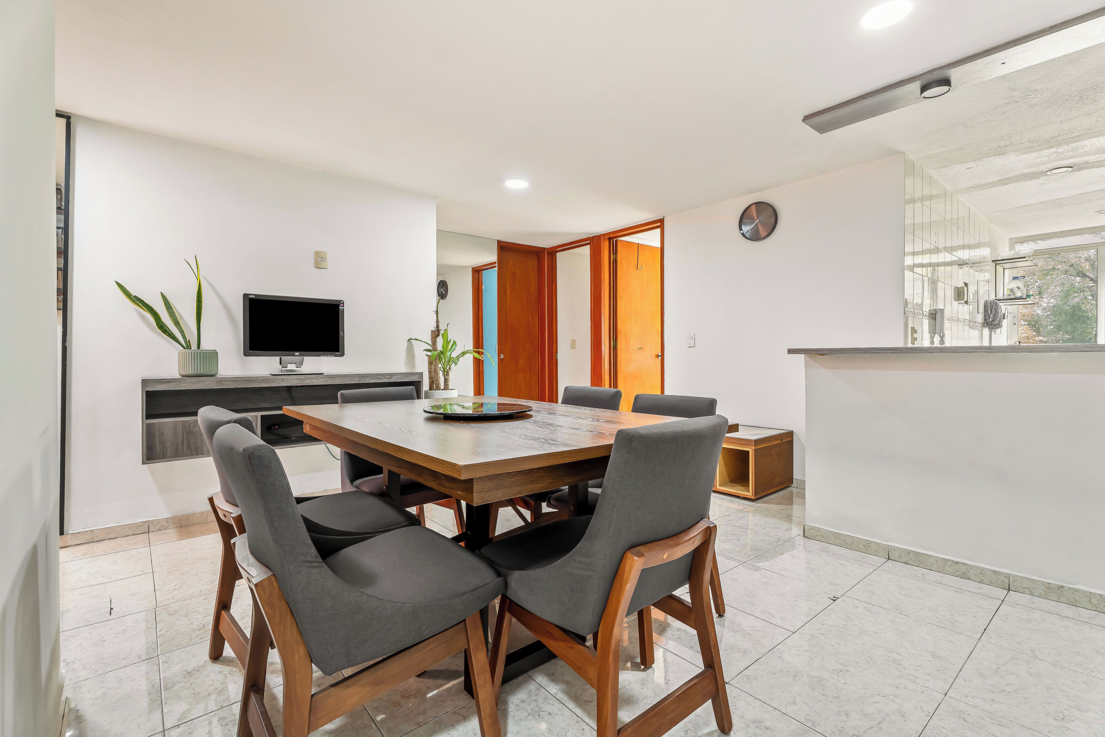 A modern dining area with a wooden table and chairs, a television, and a potted plant.