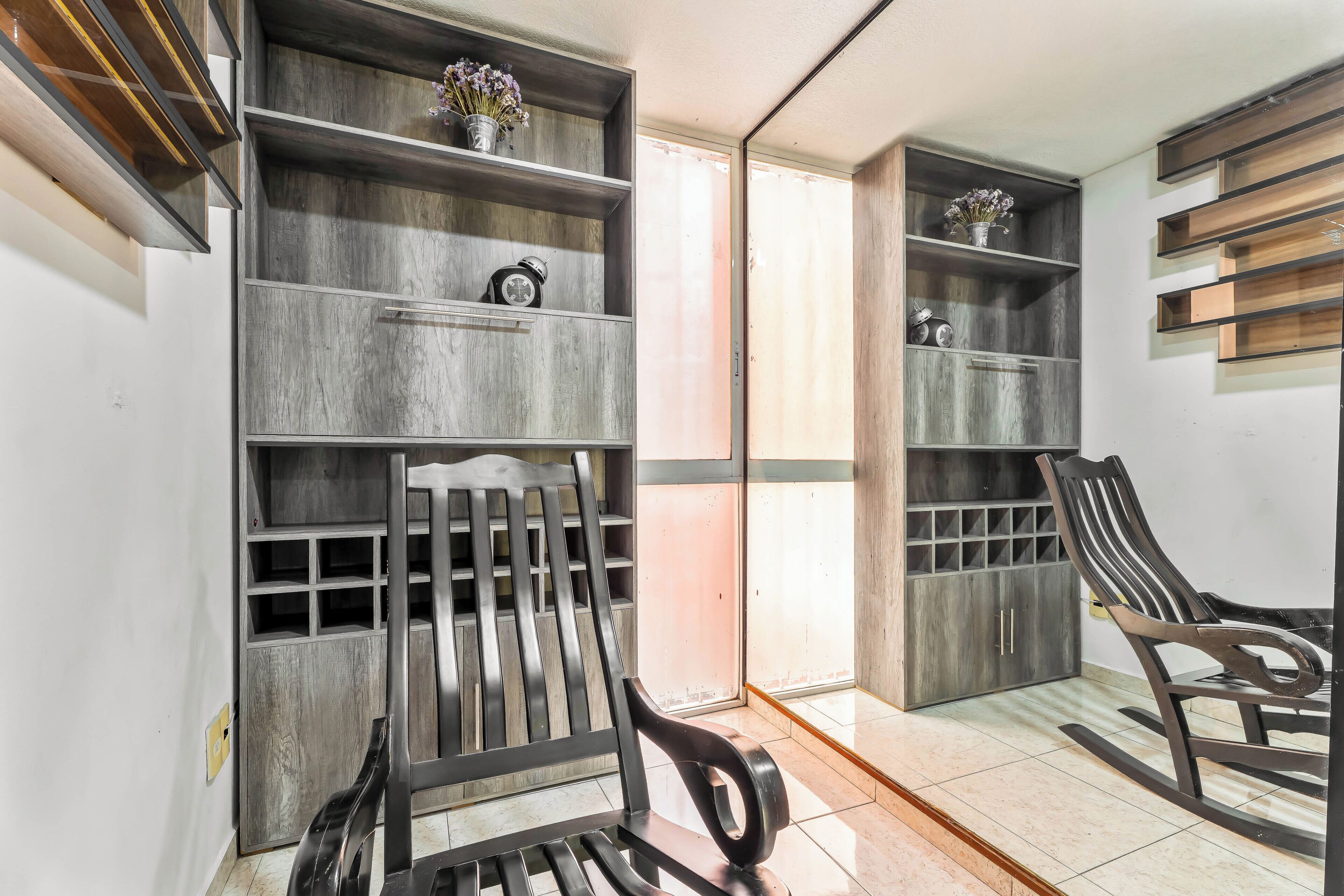 Una habitación con estanterías de madera, un sillón mecedora y una puerta que da a otra estancia.