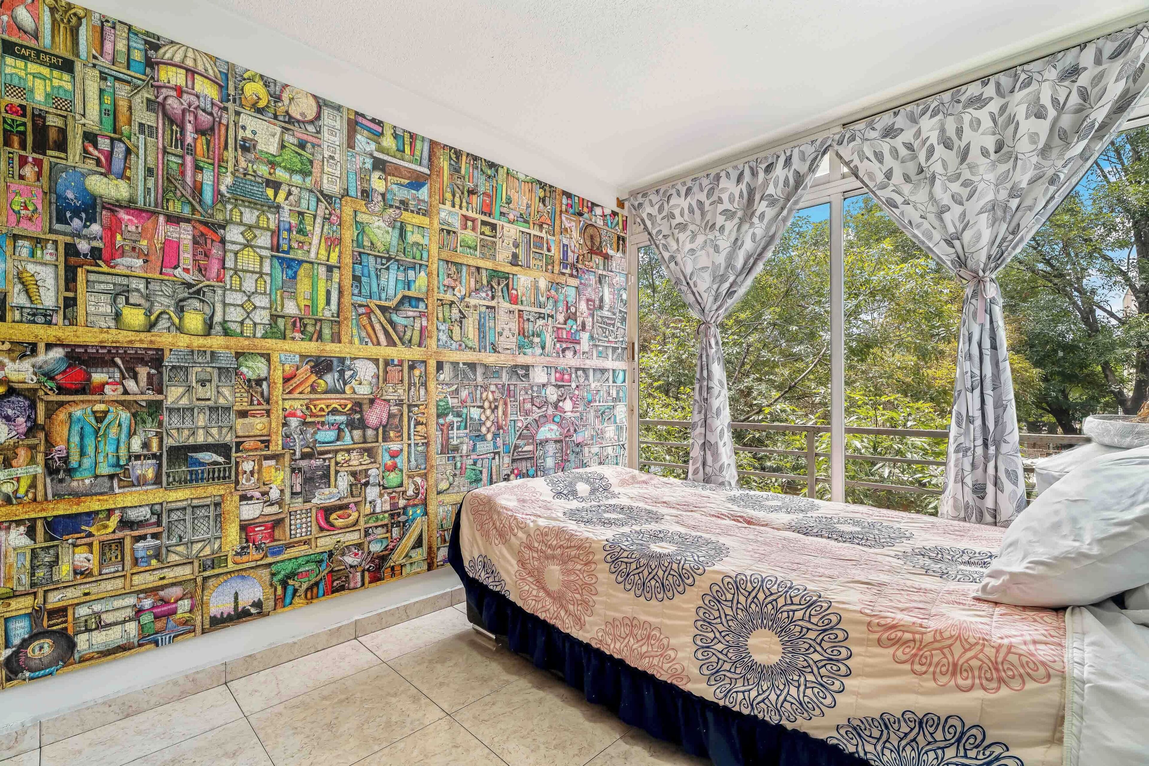 Un dormitorio con un mural grande en la pared, una cama con ropa de cama estampada y una ventana con cortinas.