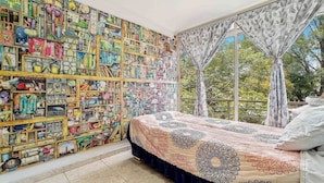 Ein Schlafzimmer mit einer großen Wandmalerei, einem Bett mit gemusterten Betttextilien und einem Fenster mit Vorhängen.