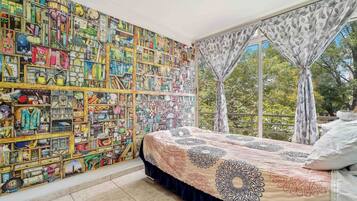 Un dormitorio con un mural grande en la pared, una cama con ropa de cama estampada y una ventana con cortinas.
