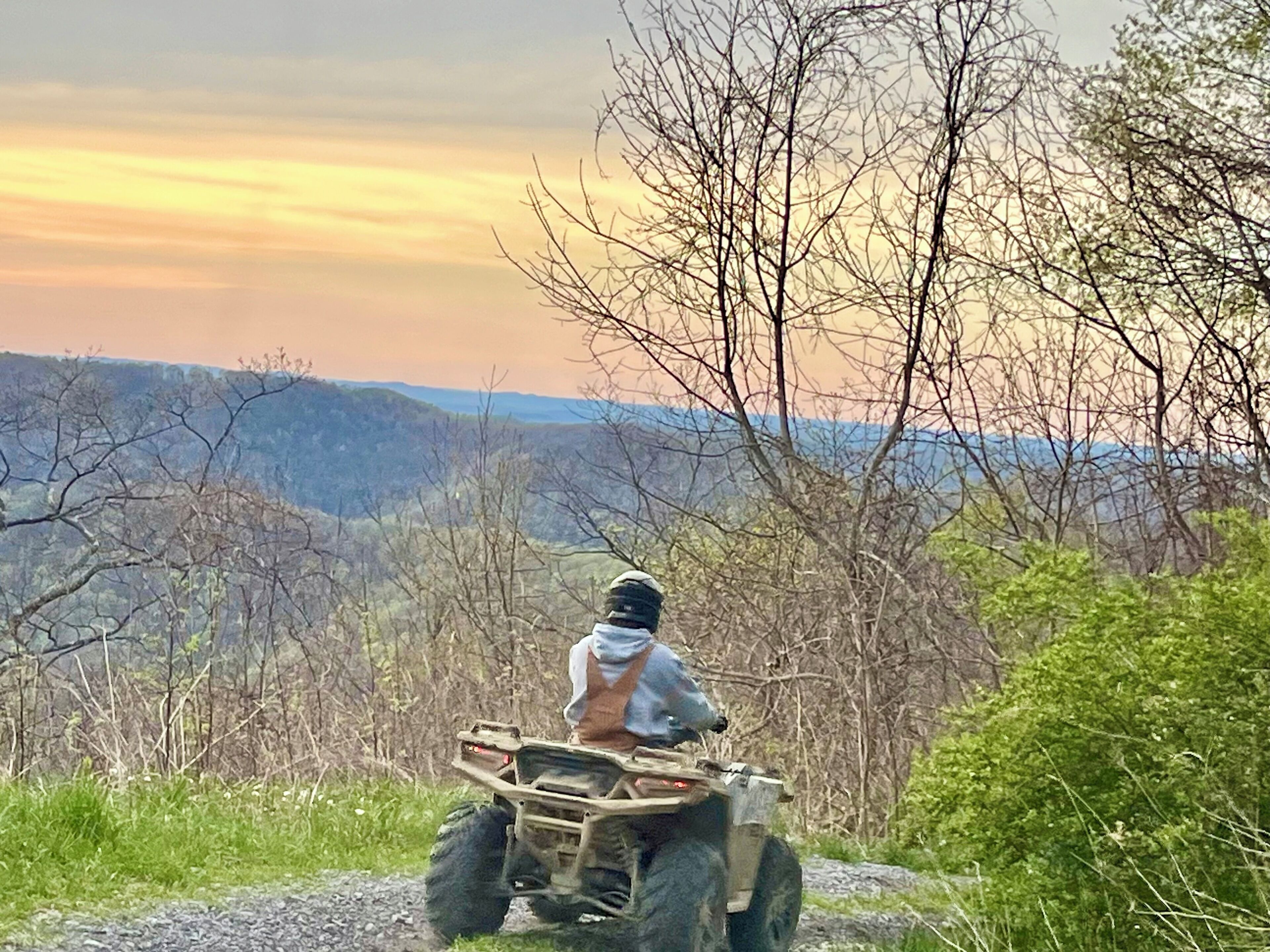 Eine Person fährt mit einem Quad auf einem Feldweg, im Hintergrund eine Berglandschaft.