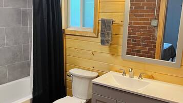 A bathroom with a bathtub, toilet, vanity with a mirror, and a window.