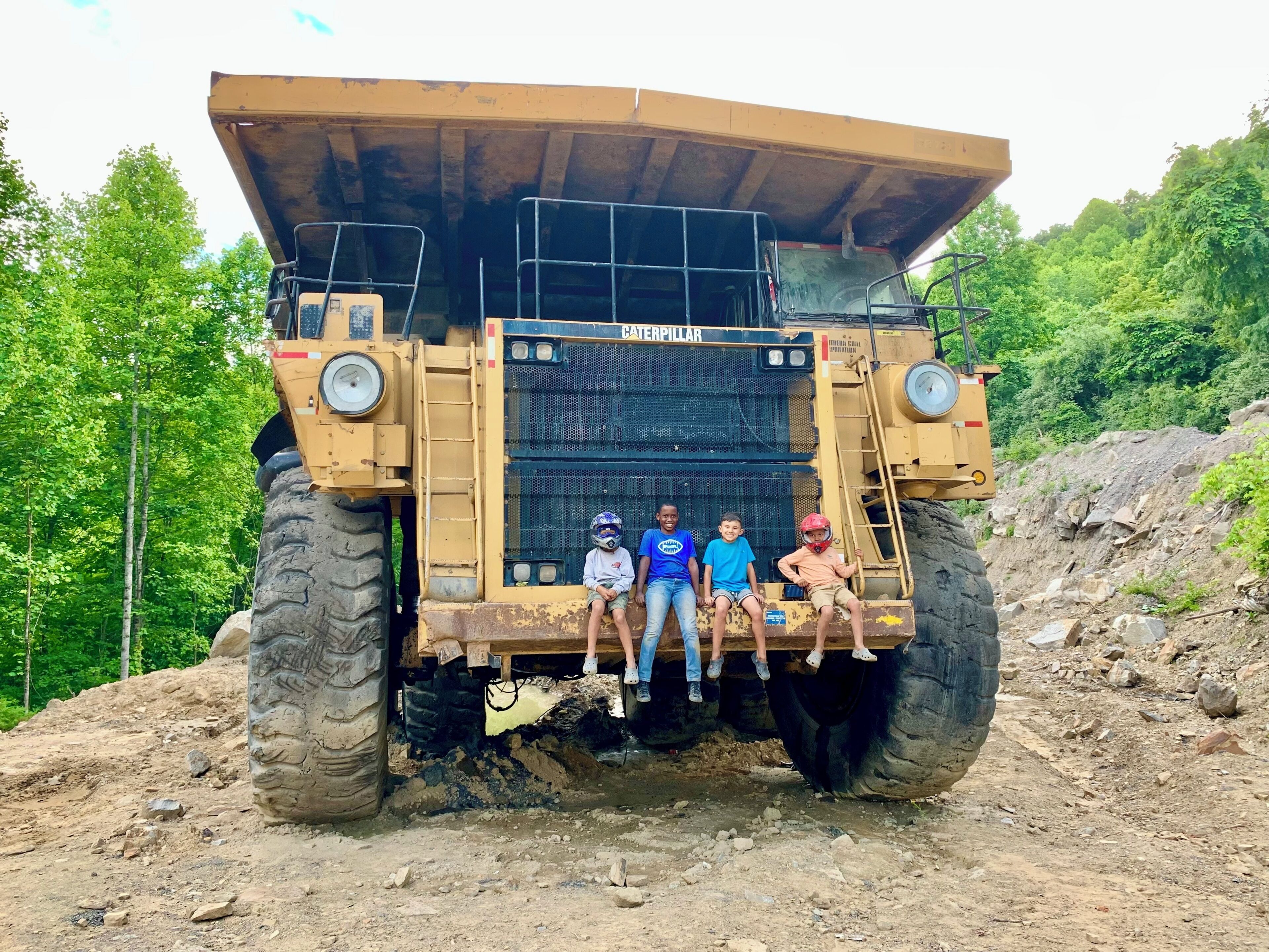 Ein großes Caterpillar Bagger mit vier Personen, die auf seiner Rückplattform sitzen.
