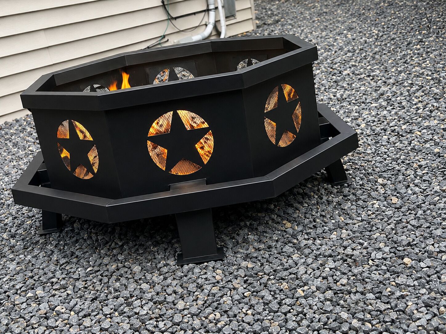 A black outdoor fire pit with circular ventilation windows and a visible flame.