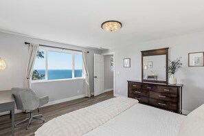 A bedroom with a large window, a bed, a desk, a chair, a dresser, and a mirror. - Harrington Reserve: Sunset Bluff • Newly Renovated Luxury Coastal Retreat • Panoramic Views • Designer Interiors • Spa Vibes (Port Angeles)