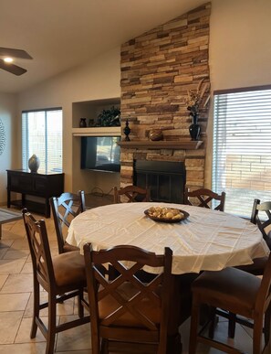 A dining area with a stone fireplace, a television, and a dining table with chairs. - Kiowa Castle - Private Pool & Hot Tub - Sleeps 14 (Lake Havasu City)