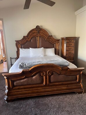 A wooden bed with a headboard, a dresser, and a ceiling fan in a room with a carpeted floor. - Kiowa Castle | Private Pool & Hot Tub | Sleeps 14 (Lake Havasu City)