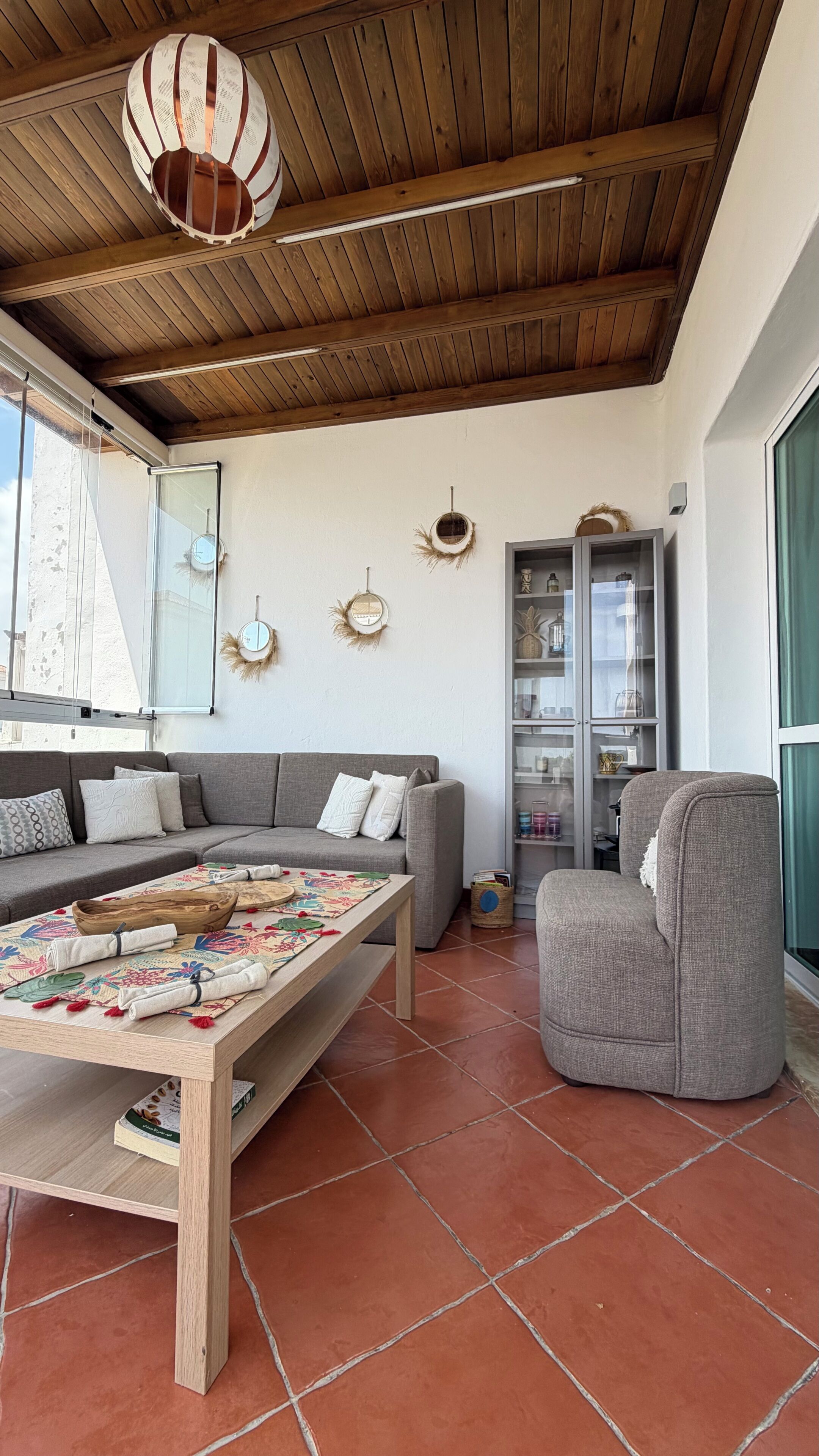 Un salon avec un plafond en bois, un canapé, une table avec un set de table et un meuble avec des portes en verre.