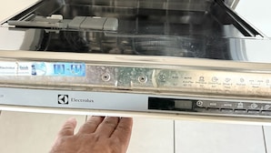 Lavastoviglie aperta con una mano che si protende verso di essa, pannello di controllo con varie impostazioni e una caramella a forma di lecca-lecca nel cestello.