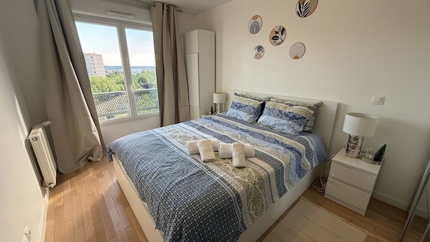 Una camera da letto con un letto grande, una finestra con tende, un termosifone, un comodino con una lampada e decorazioni alle pareti.