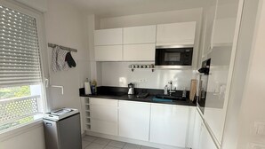 Una cucina moderna con mobili bianchi, un piano di lavoro nero, un forno a microonde integrato e un piccolo frigorifero.